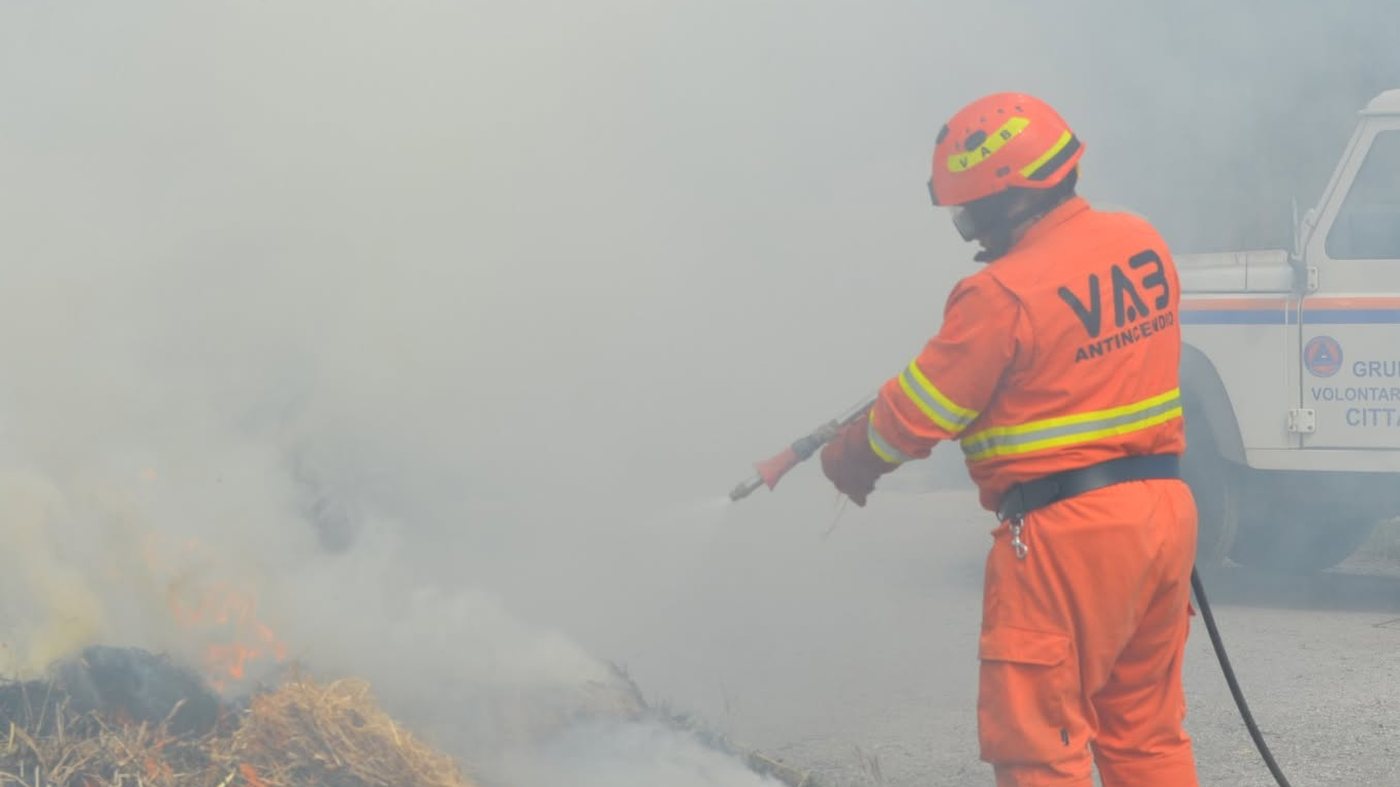 Addetto antincendio con casco e tuta ignifuga che spegne con la lancia un focolaio di paglia durante una prova pratica dei corsi Theorema
